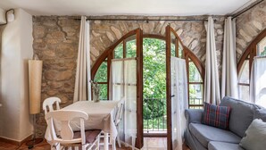 Una habitación con pared de piedra, una mesa con sillas, un sofá y una vista a través de un arco abierto.