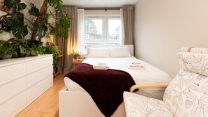 A modern bedroom with a large bed, a white dresser, and a plant wall. - Modern & Convenient 2-Bed Flat Near Tube – Heart of London (London)