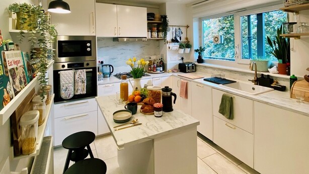 A modern kitchen with white cabinets, a central island, and a window providing natural light. - Modern & Convenient 2-Bed Flat Near Tube – Heart of London (London)