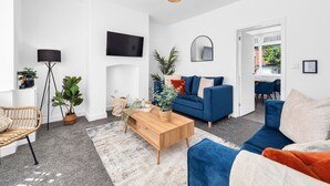Uma sala de estar moderna com um sofá azul, uma mesa de centro de madeira e uma televisão grande fixada na parede.