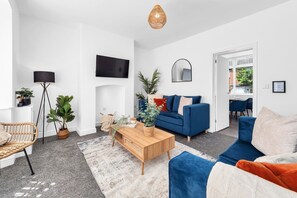 A modern living room with a blue sofa, a wooden coffee table, and a large TV mounted on the wall. - 2BDR Stanley House | Free Parking | Private Garden (Stoke-on-Trent)