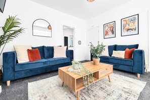 A living room with two blue sofas, a wooden coffee table, and a large plant. - 2BDR Stanley House | Free Parking | Private Garden (Stoke-on-Trent)