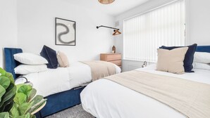Quarto com duas camas, luminária pendente, mesa de cabeceira com um vaso e uma obra de arte na parede.