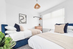 A bedroom with two beds, a hanging light fixture, a bedside table with a vase, and a wall-mounted artwork. - 2BDR Stanley House | Free Parking | Private Garden (Stoke-on-Trent)