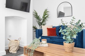 A living room with a blue sofa, a wooden coffee table, and a TV mounted on the wall. - 2BDR Stanley House | Free Parking | Private Garden (Stoke-on-Trent)