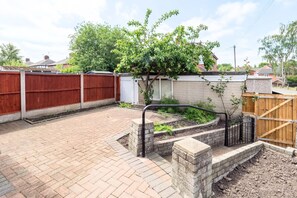 A paved backyard with a brick patio, a wooden fence, a small tree, and a white shed. - 2BDR Stanley House | Free Parking | Private Garden (Stoke-on-Trent)