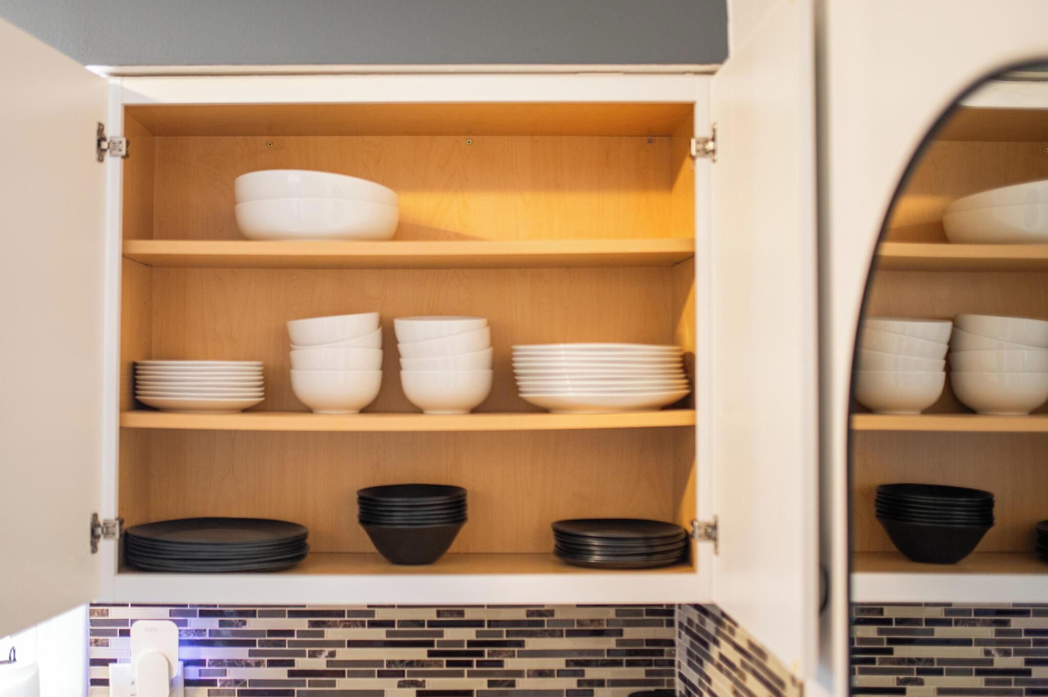 A kitchen cabinet with shelves holding white and black bowls and plates.