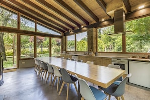 Eine geräumige Küche mit großen Fenstern, einem langen Holztisch und modernen Stühlen.