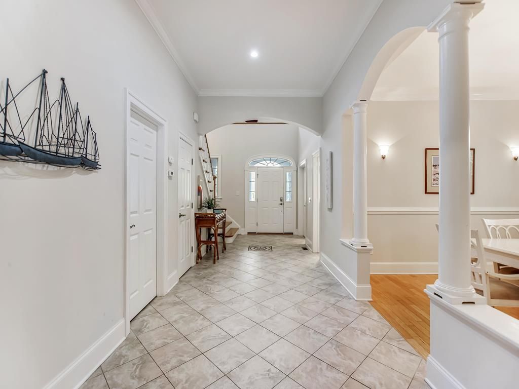 A hallway with white walls, a tiled floor, and a staircase leading to another room.
