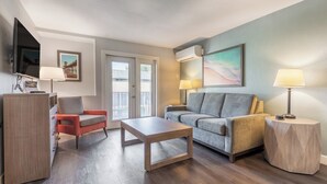A living room with a grey sofa, a red armchair, a wooden coffee table, and a TV mounted on the wall.