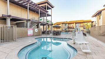 A swimming pool with a slide, outdoor seating, and a covered area with stairs.
