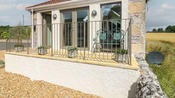 A small stone building with a tiled roof, large glass doors, and a balcony with metal railings and potted plants. - The Barn, Romantic Countryside Escape near St Andrews (Cupar)