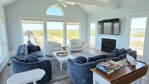 A spacious living room with a high ceiling, large windows, and a fireplace. - Spacious Beach House | Decks & Pool + Beach Nearby (Bethany Beach)