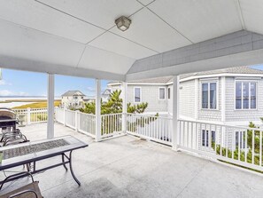 A covered patio area with a table and chairs, a white fence, and a view of neighboring houses. - Spacious Beach House | Decks & Pool + Beach Nearby (Bethany Beach)