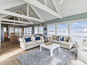 Ein geräumiges Wohnzimmer mit hoher Decke, großen Fenstern, einer Küchenzeile und Blick auf das Wasser.