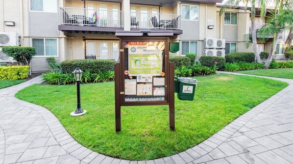 Un tablón de anuncios con información en un área verde frente a un edificio.
