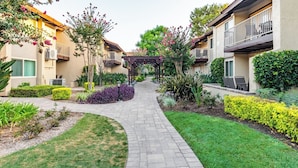A courtyard with a paved walkway, surrounded by well-maintained gardens and residential buildings with balconies. - Anaheim | Romantic Disney Retreat | Pool + Parks (Anaheim)