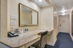 Zona de recepción de hotel con mostrador de mármol, teléfono, espejo y dos botellas de agua.