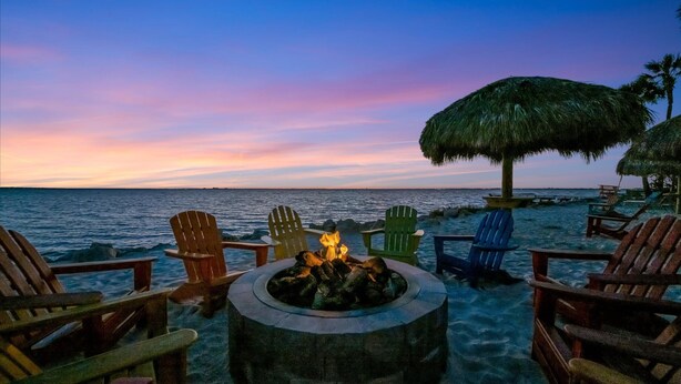 A beachside seating area with a fire pit and chairs, overlooking the ocean. - Sunset Cove – Tampa Sunsets from Your Balcony (Tampa)
