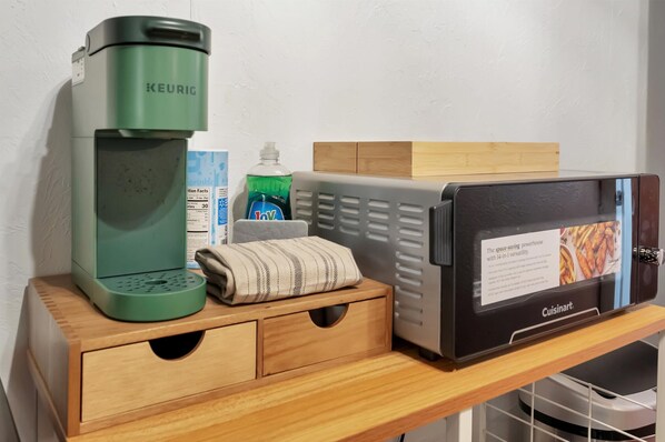Pieni keittiönurkkaus, jossa on Keurig-kahvinkeitin, Cuisinart-leivänpaahdin, pullo astianpesuainetta ja siististi taitettu pyyhe puisen työtason päällä.