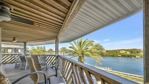 A covered outdoor seating area with wicker chairs and a view of a lake and palm trees. - Beachfront 3B Condo | Walk right onto the sand! (Indian Rocks Beach)