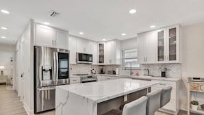 A modern kitchen with white cabinetry, stainless steel appliances, a marble island, and bar stools. - Beachfront 3B Condo | Walk right onto the sand! (Indian Rocks Beach)