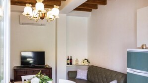 Ein gemütliches Wohnzimmer mit Fernseher, einer Couch, einem Esstisch mit Stühlen und einer Pendelleuchte.