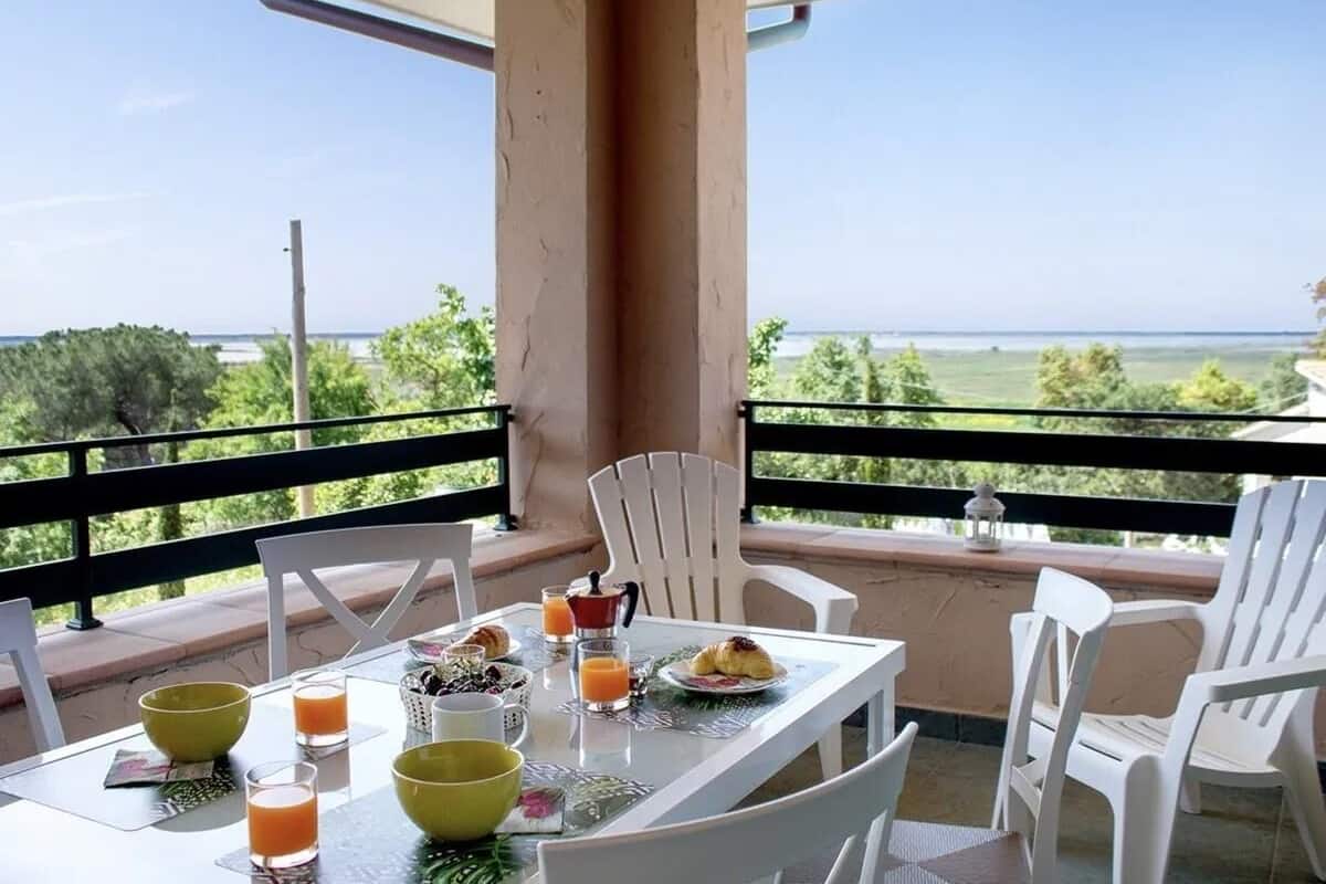 Un balcón con mesa dispuesta para el desayuno, sillas blancas y vista al mar.