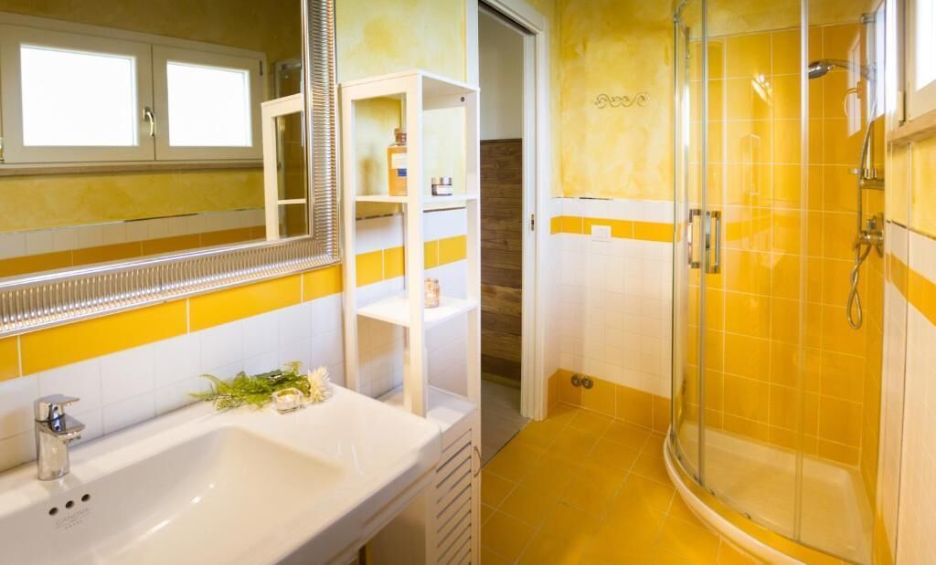 A bathroom with a white sink, mirror, and yellow-tiled shower enclosure.