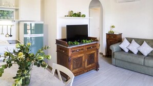 Ein gemütliches Wohnzimmer mit einem Holzschrank, einem Fernseher, einem grünen Sofa und einem Essbereich mit einem weißen Stuhl und Tisch.