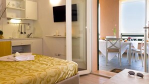 Ein Schlafzimmer mit Bett, Fernseher, Badezimmer mit Spiegel sowie Essbereich mit Tisch und Stühlen.