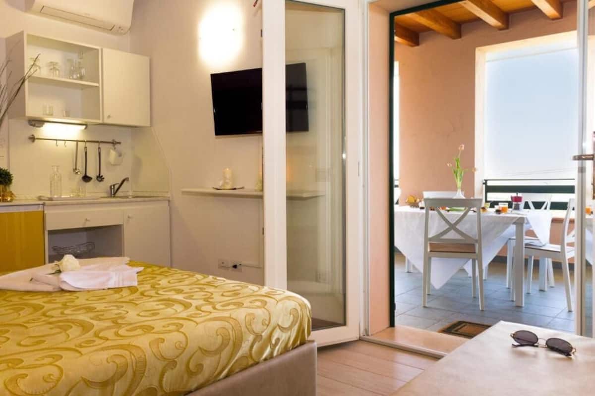 Un dormitorio con cama, televisor, baño con espejo y zona de comedor con mesa y sillas.