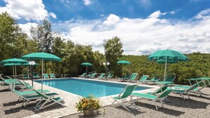 A swimming pool with green lounge chairs and umbrellas, surrounded by trees and a clear sky. - Tenuta della Selva - Castellaccio 7 (Murlo)