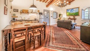 A spacious kitchen with wooden beams, a dining area with a large table and chairs, a living room with a sofa, and a painting on the wall. - Tenuta della Selva - Castellaccio 7 (Murlo)