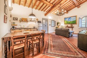A spacious kitchen with wooden beams, a dining area with a large table and chairs, a living room with a sofa, and a painting on the wall. - Tenuta della Selva - Castellaccio 7 (Murlo)