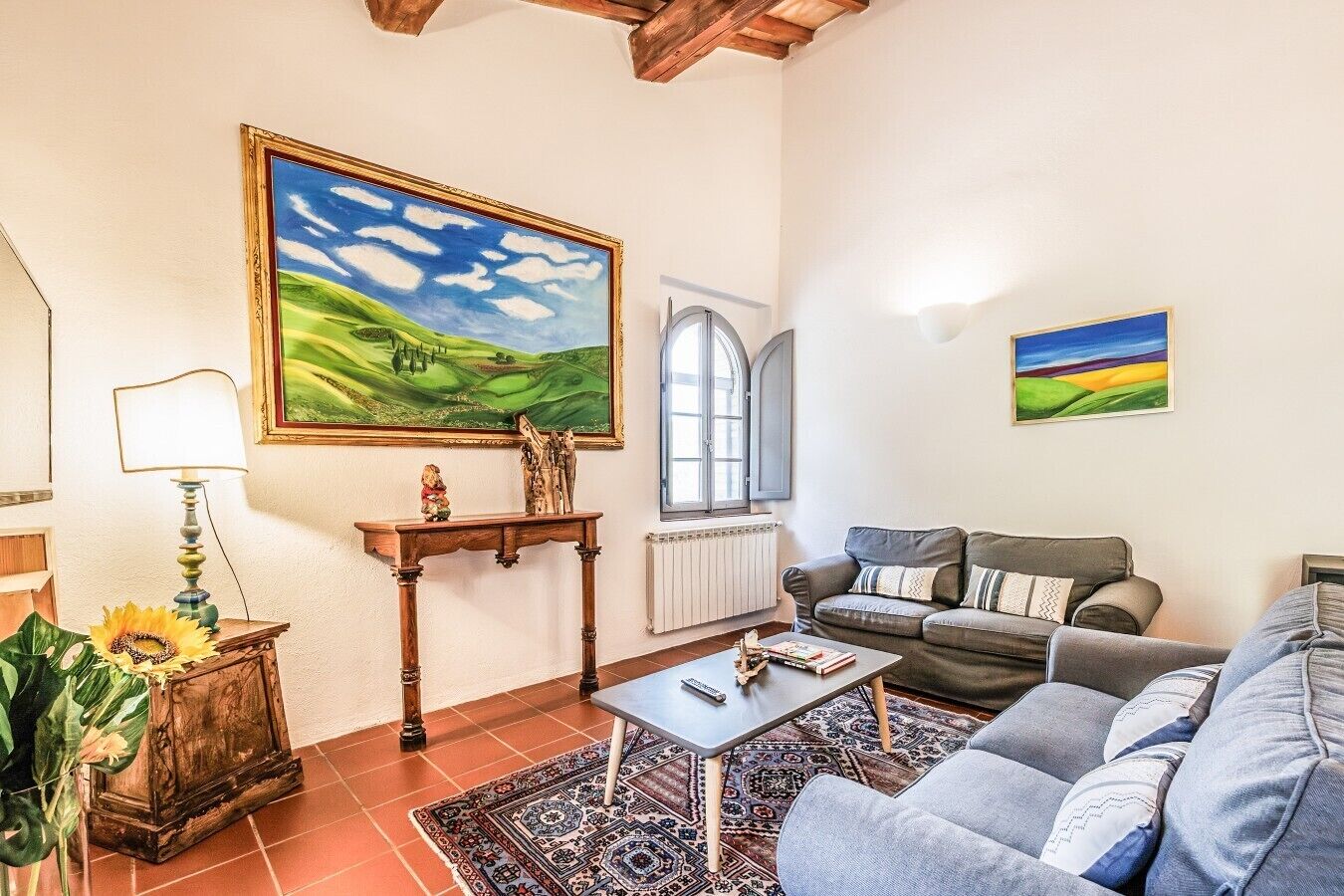 Una sala de estar con un sofá, una mesa de centro, una lámpara, un cuadro y una ventana.