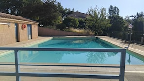 Una piscina rectangular amb terrassa enrajolada, envoltada per un mur baix i arbres.
