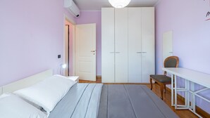 Un dormitorio con cama, mesita de noche, silla, armario y una lámpara colgante.