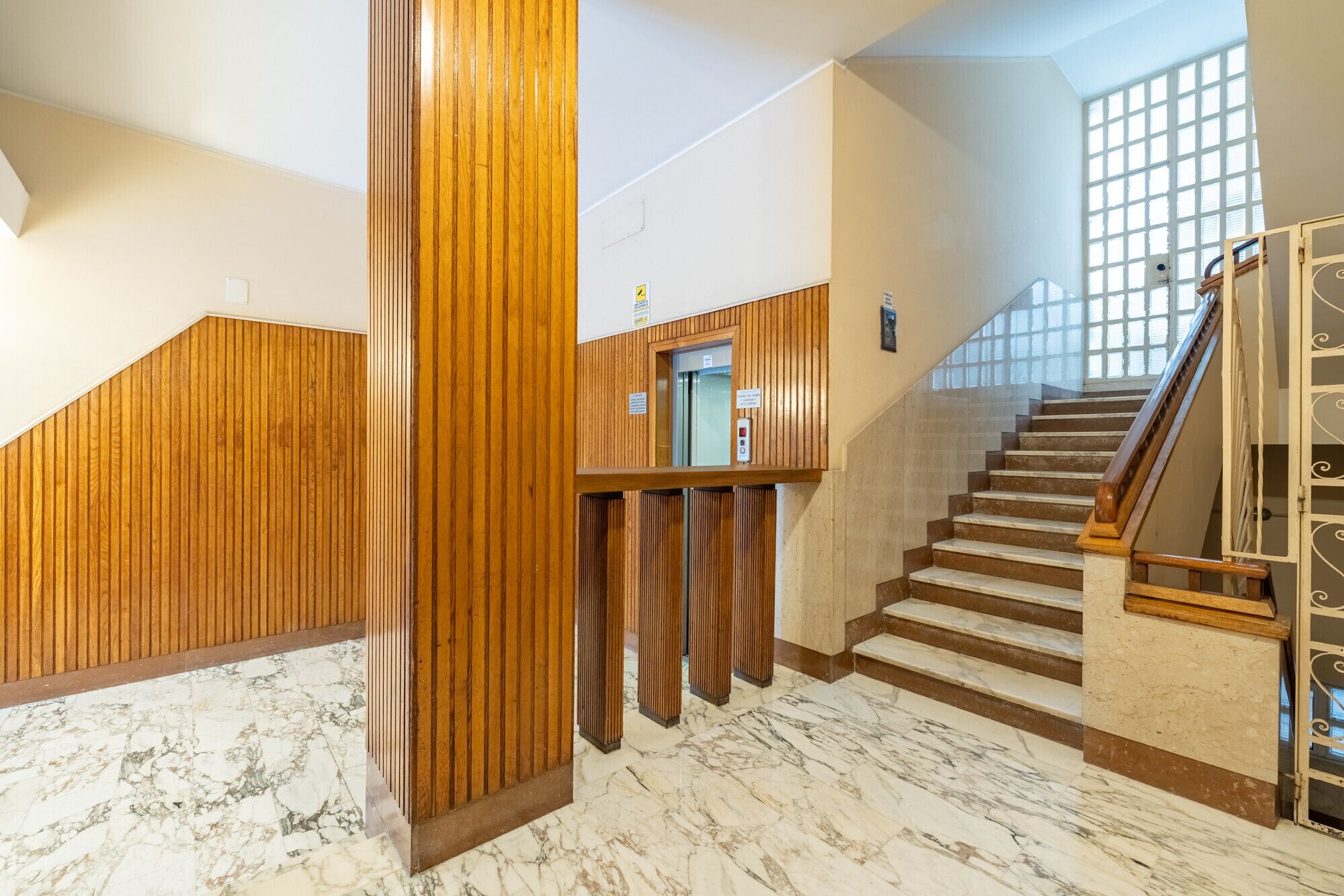A modern interior with a marble floor, wooden paneling, and a staircase with a glass railing.