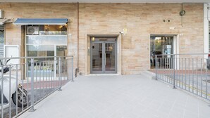 Entrada de un edificio con suelo de baldosas, barandillas de metal y puerta de cristal.