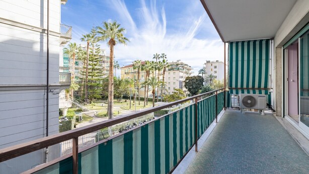 Un balcón con un aire acondicionado Samsung, un toldo a rayas verde y blanco, y vistas a palmeras y edificios.