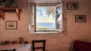 A room with a view of the sea through an open window, a table with a white tablecloth, a chair, and a red cushion. - Tsoupis Villa (Kentroma)