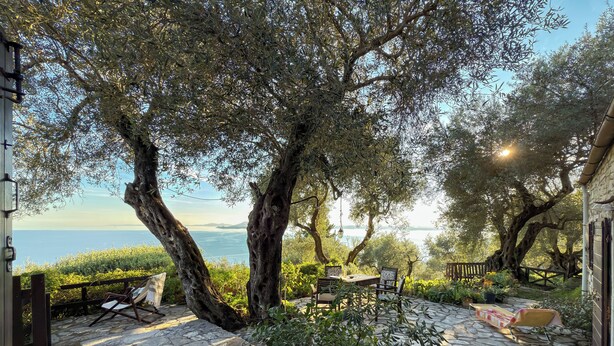 A stone patio with outdoor furniture, a view of the sea, and olive trees. - Tsoupis Villa (Kentroma)