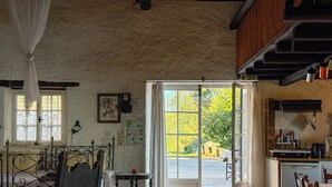 A rustic room with a bed, a small table, a chair, and a window with curtains. - Tsoupis Villa (Kentroma)