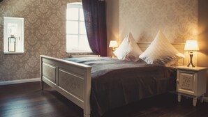 Une chambre à coucher avec un lit, deux tables de chevet avec des lampes, une fenêtre avec des rideaux et un papier peint à motifs.