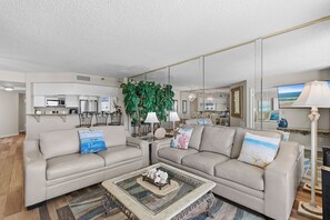 A modern living room with a sofa, coffee table, and a large plant. - 🌊Gorgeous Ocean Views | Oceanfront Complex | Sand Dollar 1105🌊 (Daytona Beach Shores)