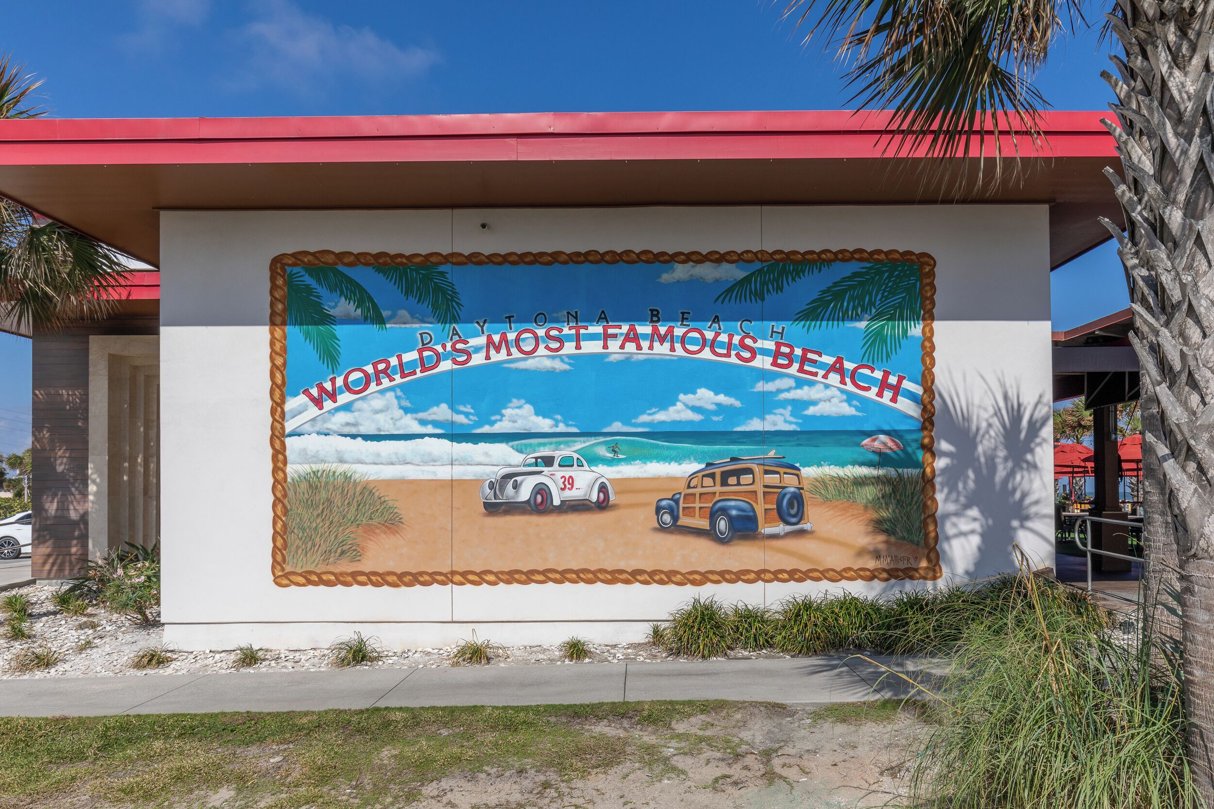 Un mural en un edificio con el texto "Daytona Beach World's Most Famous Beach" y una escena de playa que muestra un coche y un camión.