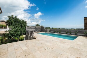 A swimming pool with a tiled deck, surrounded by greenery and a clear sky. - Villa Ulivi 10 – Is Molas Golf Resort (Is Molas)