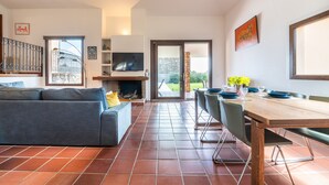 Un soggiorno con divano, televisore, camino, tavolo da pranzo, sedie e vista panoramica tramite vetrate.