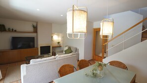 A modern living room with a flat-screen TV, sofa, dining table, wicker chairs, and a staircase. - Daró 3D 03 Corner house with air conditioning, pool, close to the beach (Torroella de Montgri)